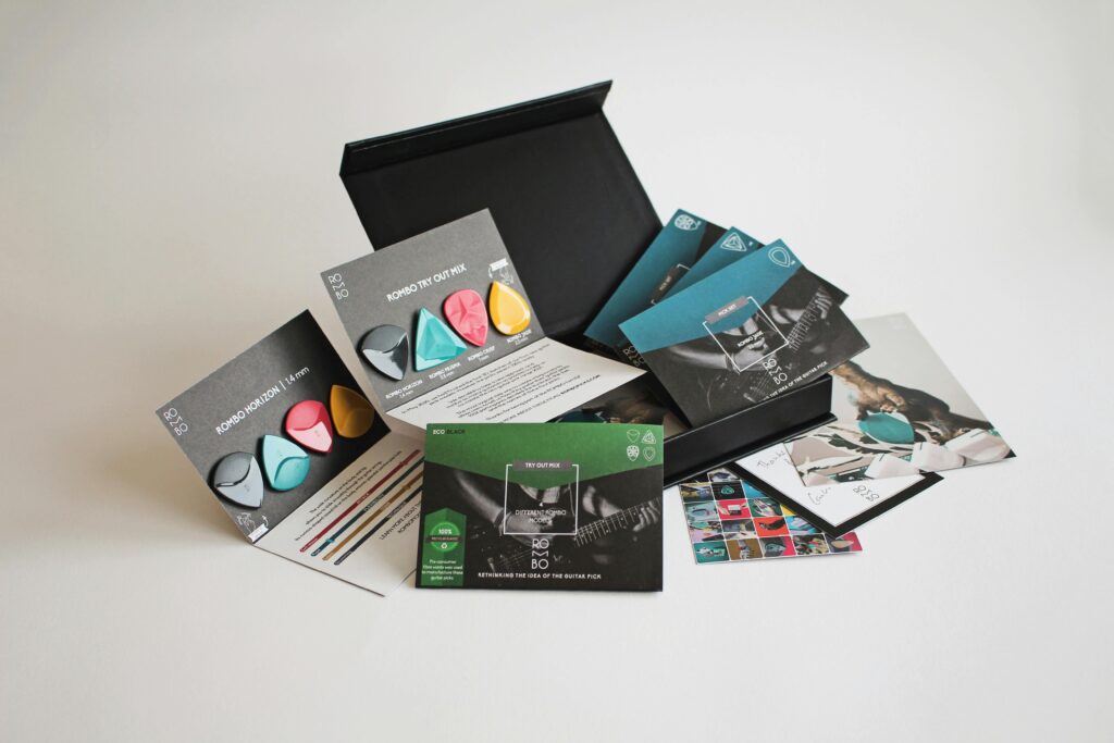 A variety pack of colorful guitar picks with packaging and promotional materials.